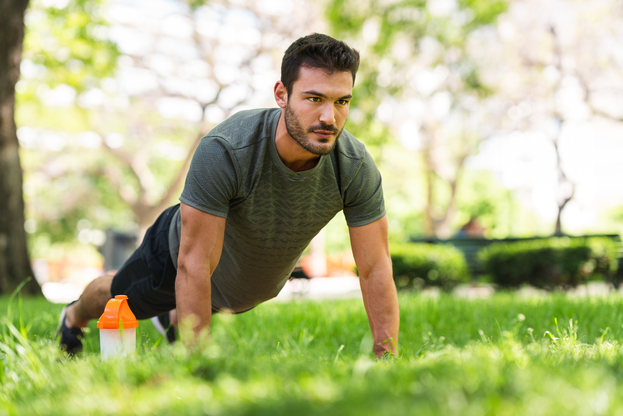 A young man doing a push-up in a park.