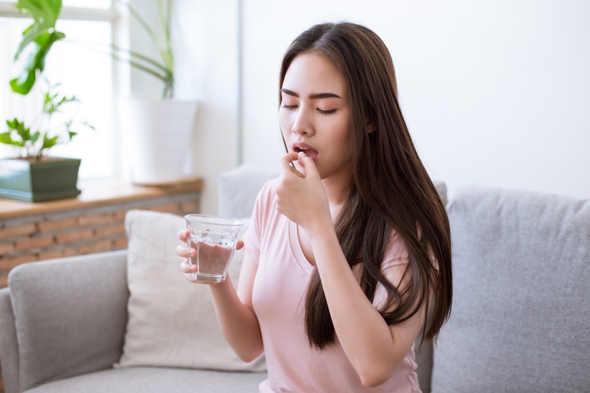 Sick young woman taking pills while sitting on the sofa at home