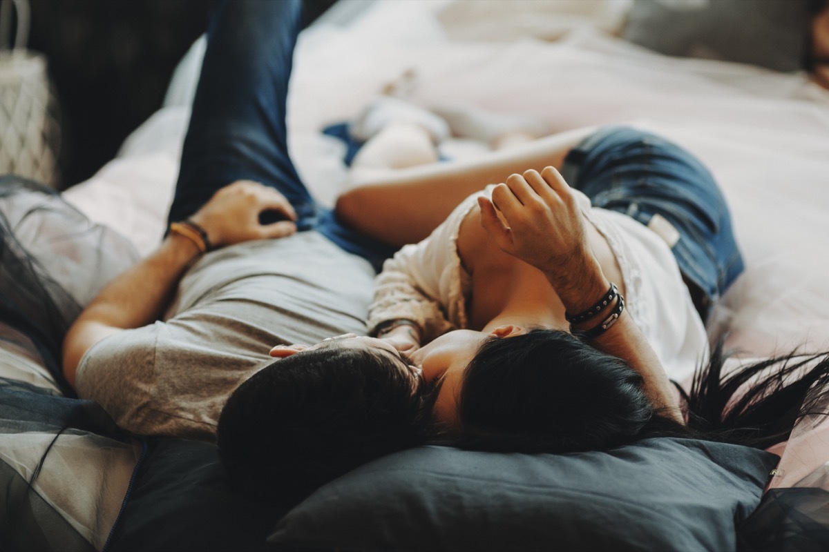 attractive romantic couple laying on bed ,hugging and kissing in a cozy room.