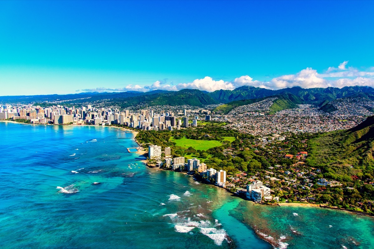 The entire coastline of Honolulu, Hawaii including the base of Diamond Head crater and state park, past the hotel lined Waikiki Beach towards downtown in the distance including the suburban neighborhoods dotting the hills surrounding the city center.