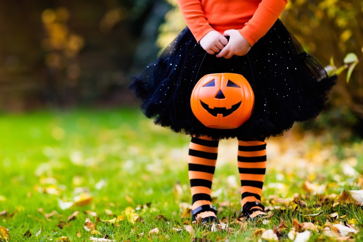 little girl holding trick or treating pumpkin on halloween