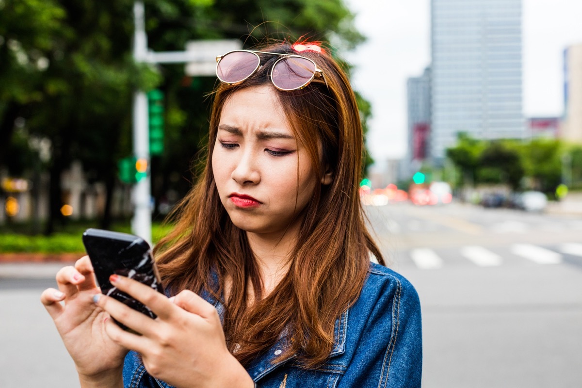 young asian woman looking disappointed while she uses her phone on the street