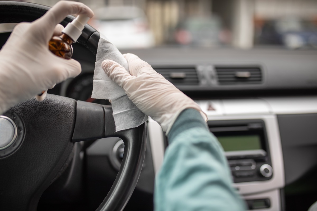 Person disinfecting and cleaning car interior with antiseptic liquid and wet disinfection wipes. Steering wheel is one of dirtiest parts in car and can contains viruses and bacteria.