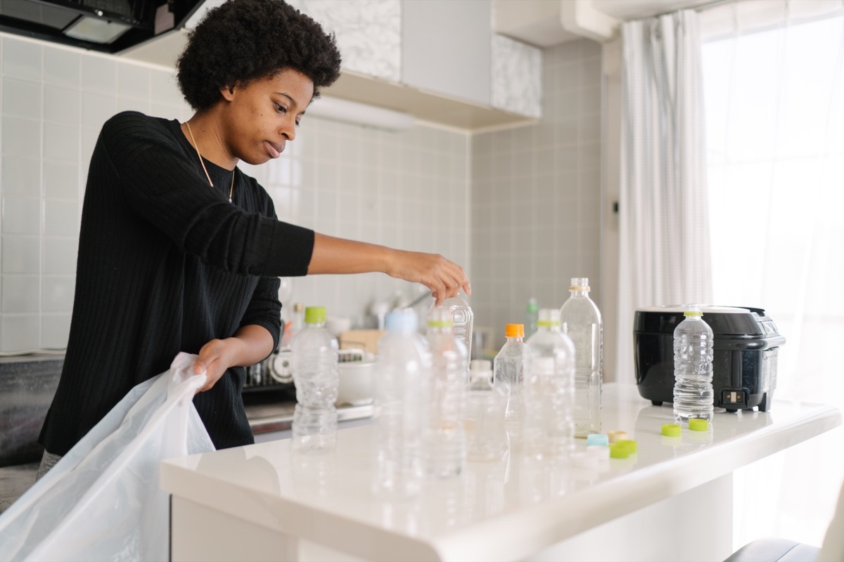 A young woman is separating wastes and pet bottles at home for recycling.