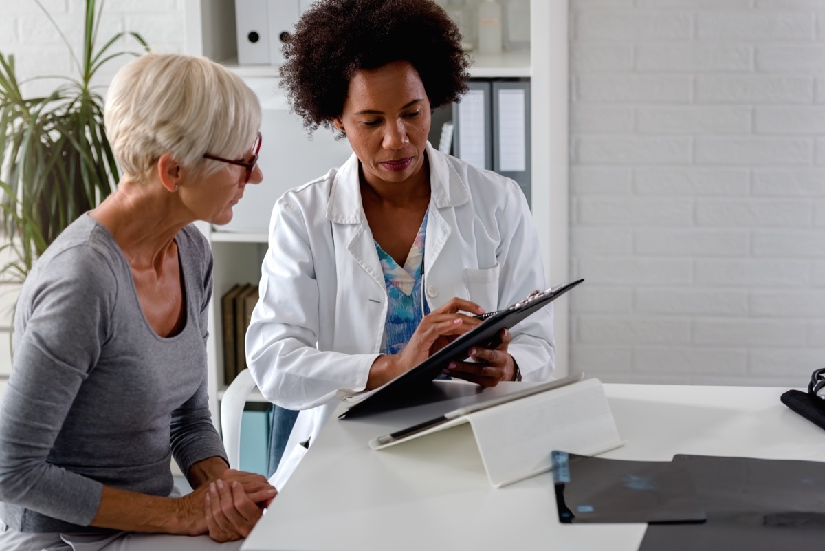 A female doctor sits at her desk and chats to an elderly female patient while looking at her test results