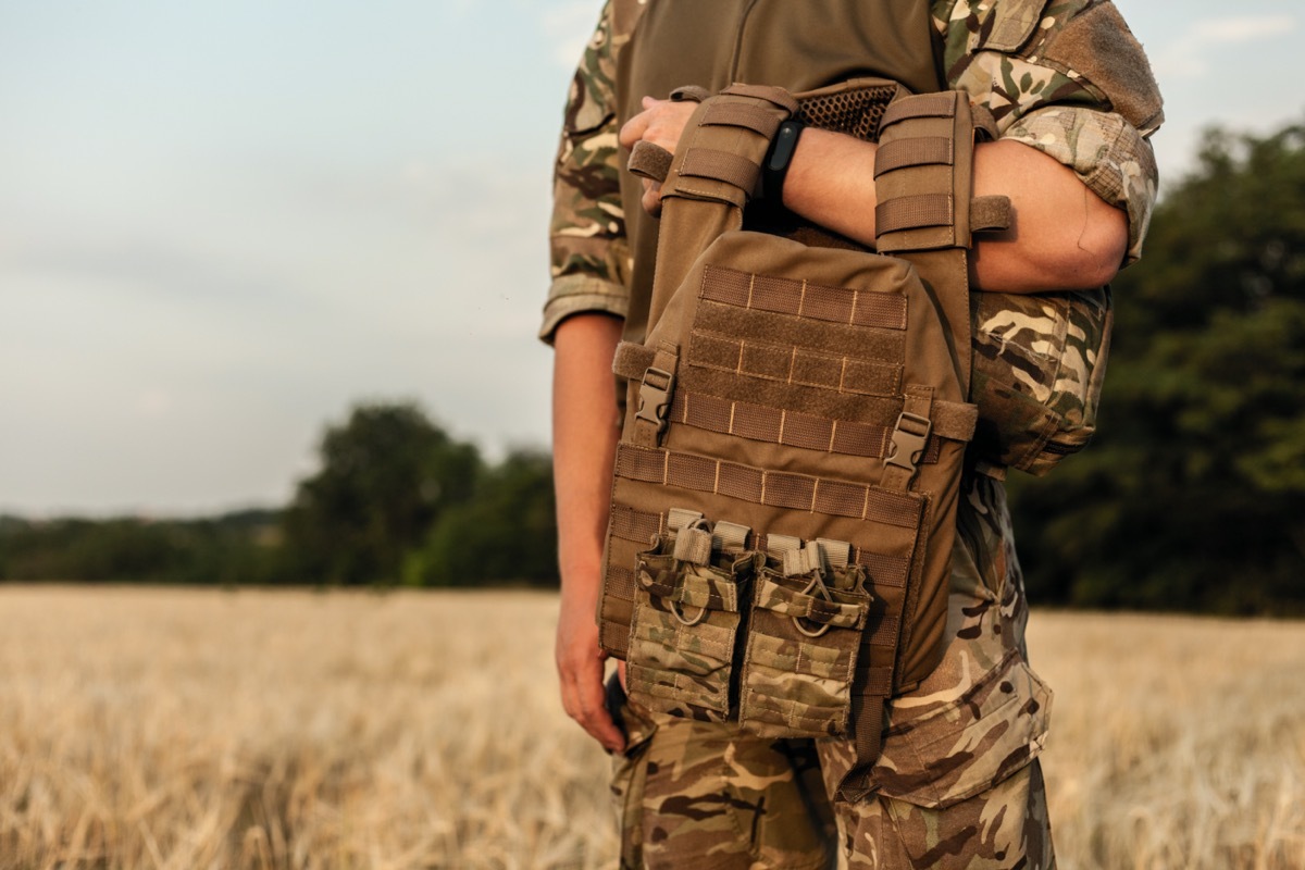 military man standing in the filed in his outfit and with a bulletproof vest