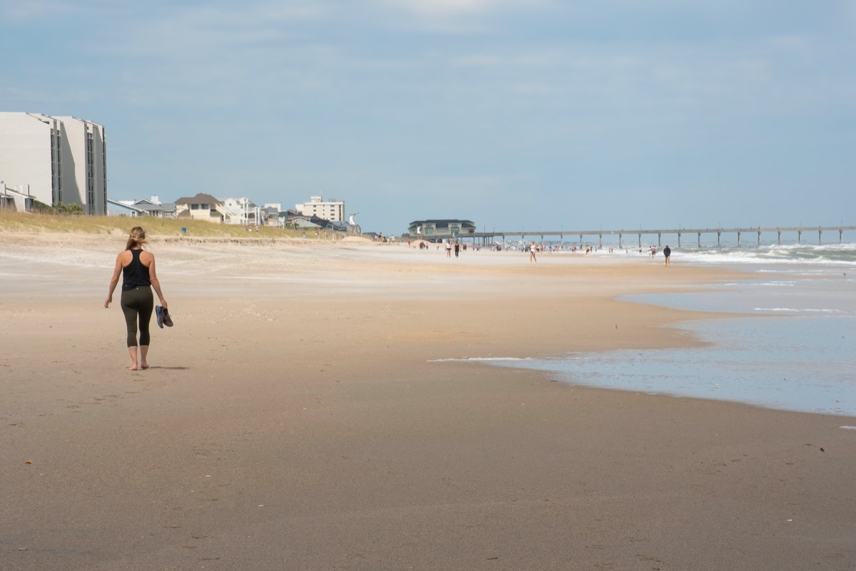 A young woman walks along a sparsely populated beach amid COVID-19.