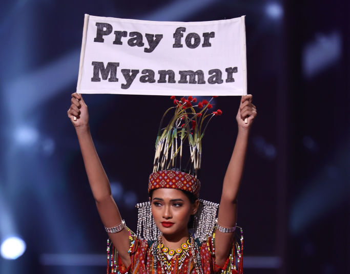 Miss Myanmar Ma Thuzar Wint Lwin competing in the 2021 Miss Universe pageant while holding up a sign that says 