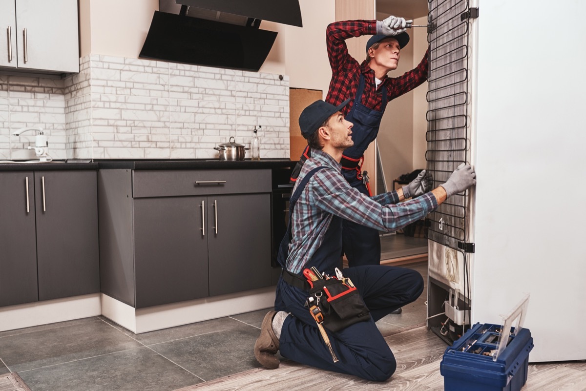 Two handymen with refrigerator. men mechanics checking refrigerator with screwdriver. They assist each other. Side view