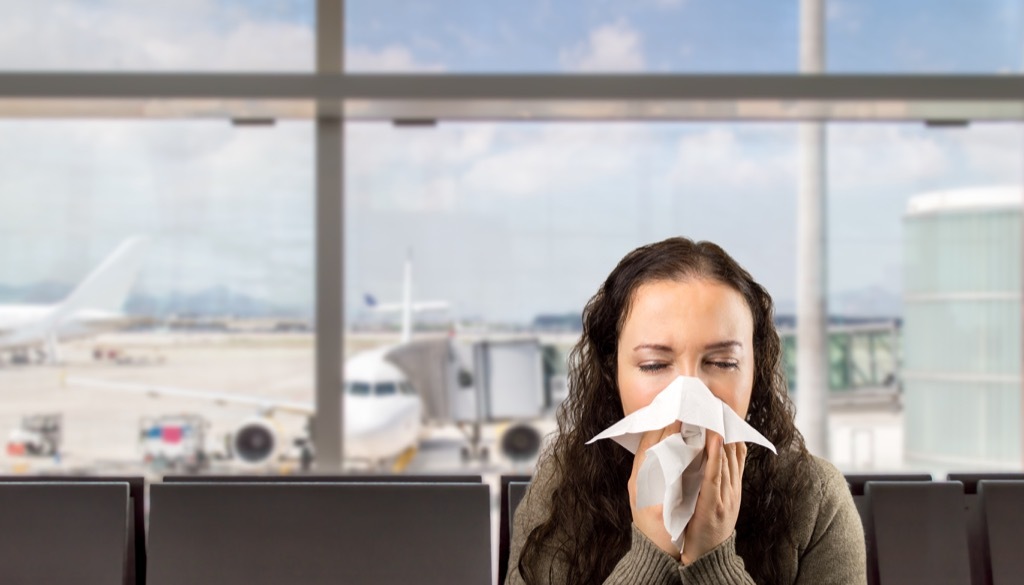 Woman sneezing at the airport {What to Do If You Have the Flu}