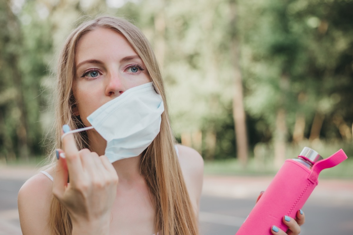 Woman taking off her respiratory mask and holding a bottle of water