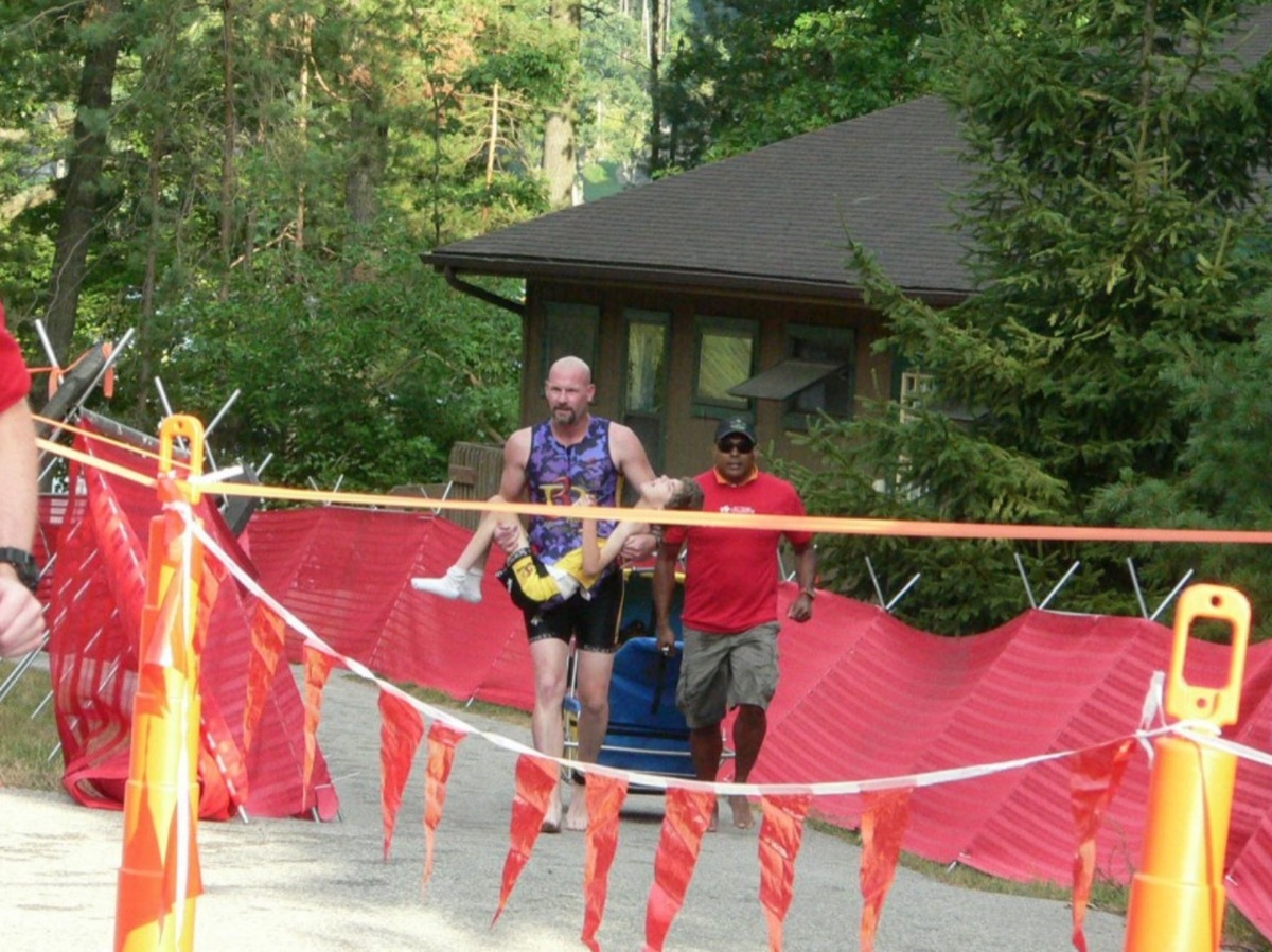 white father carrying daughter across finish line of race