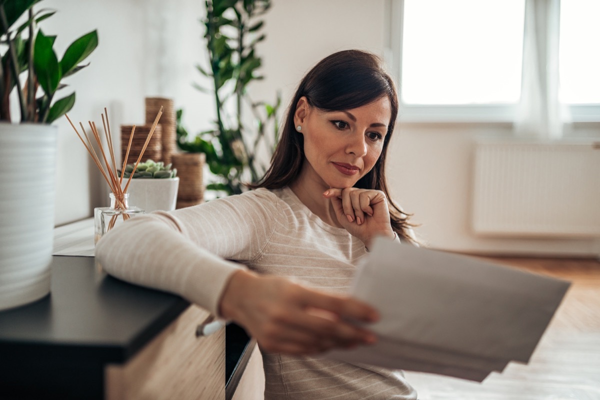 Pensive woman looking at received mail at home, holding blank envelopes.