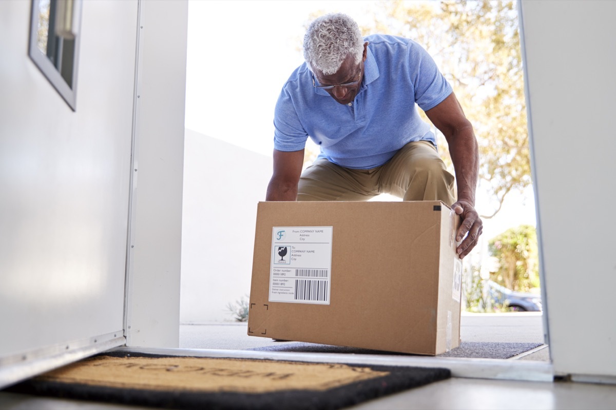 Senior Man Coming Back To Home Delivery In Cardboard Box Outside Front Door