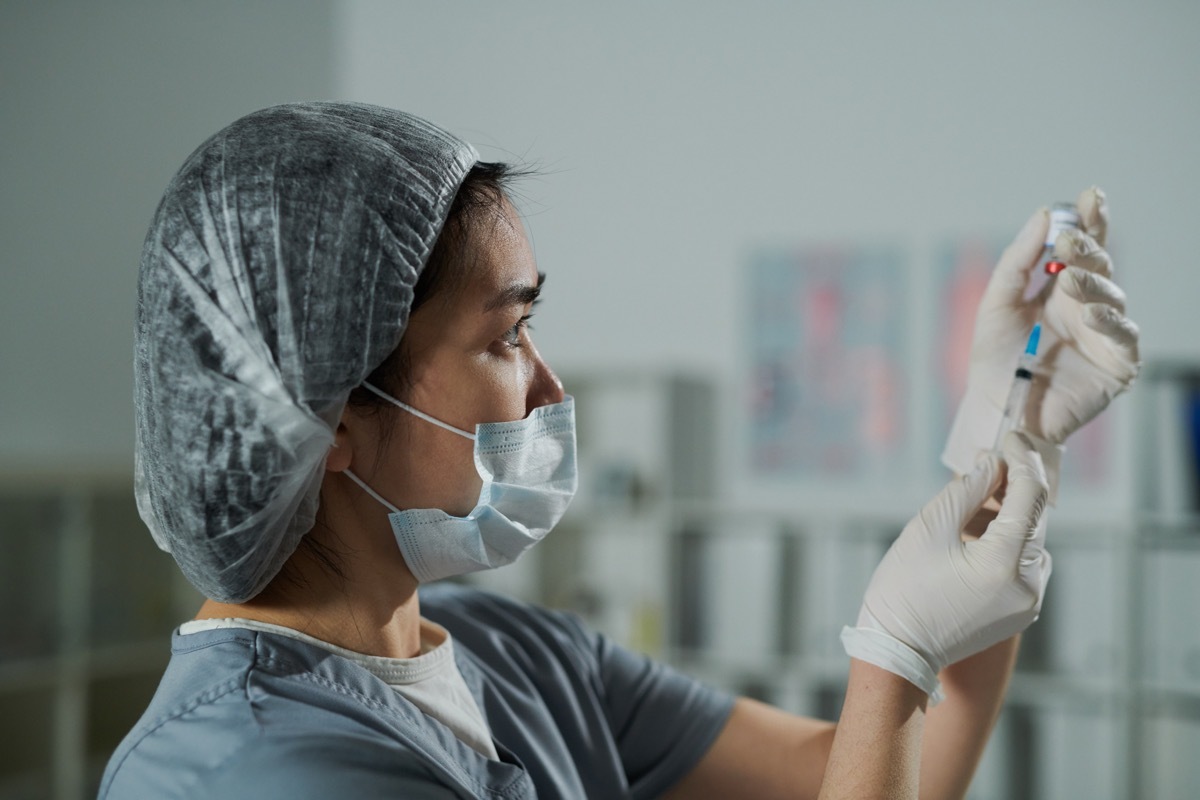 protective workwear preparing injection for patient in medical office of contemporary clinics