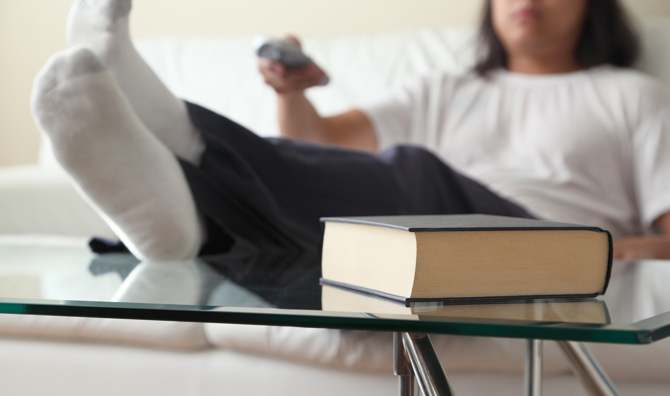 A man sitting with his feet on top of a glass coffee table next to a book.