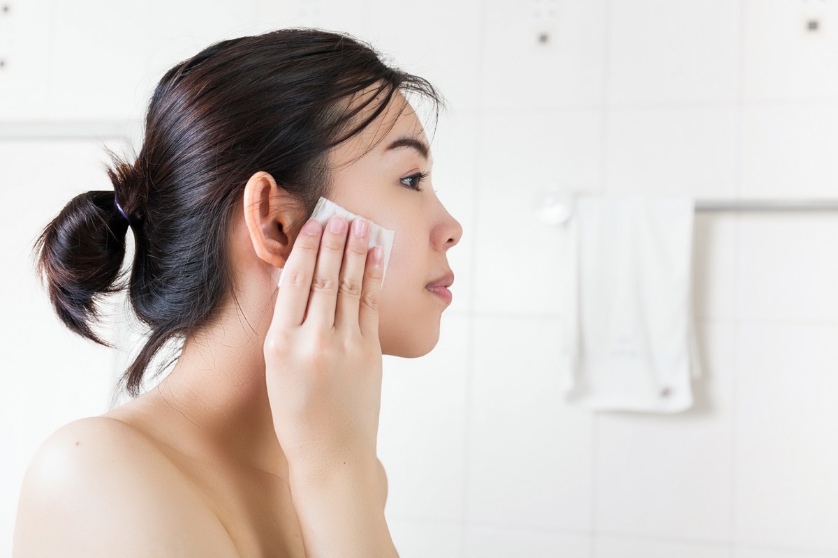 young asian woman removing makeup with wipe