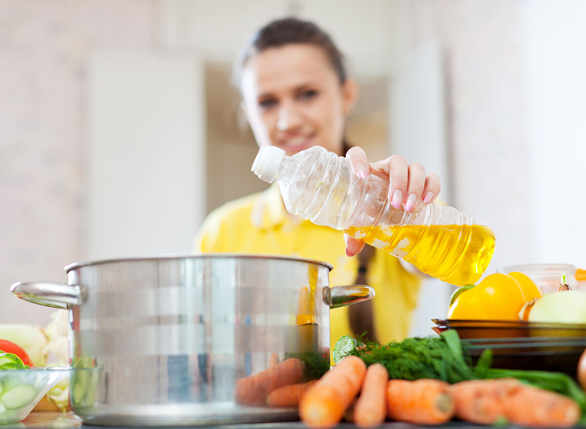 woman adding oil to cooking pot