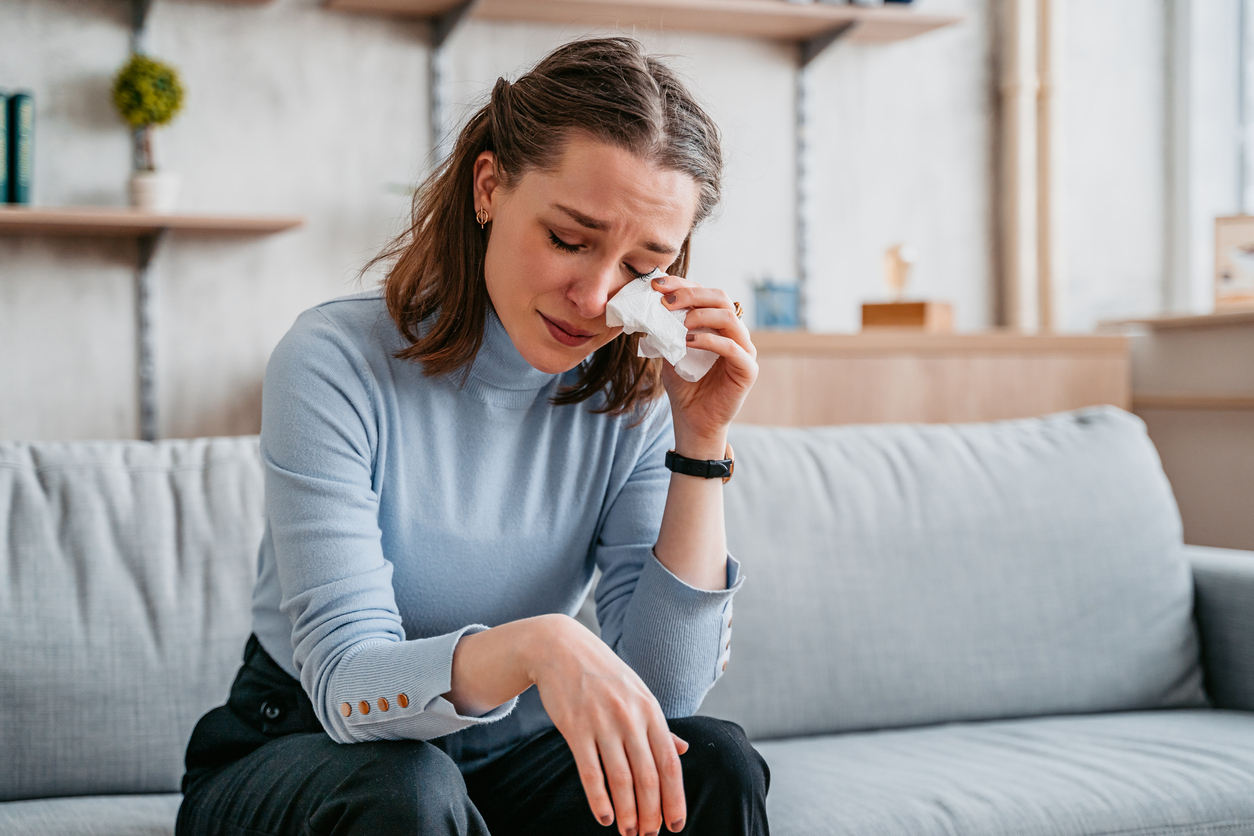 Beautiful young woman sitting on the sofa in the living room and crying.