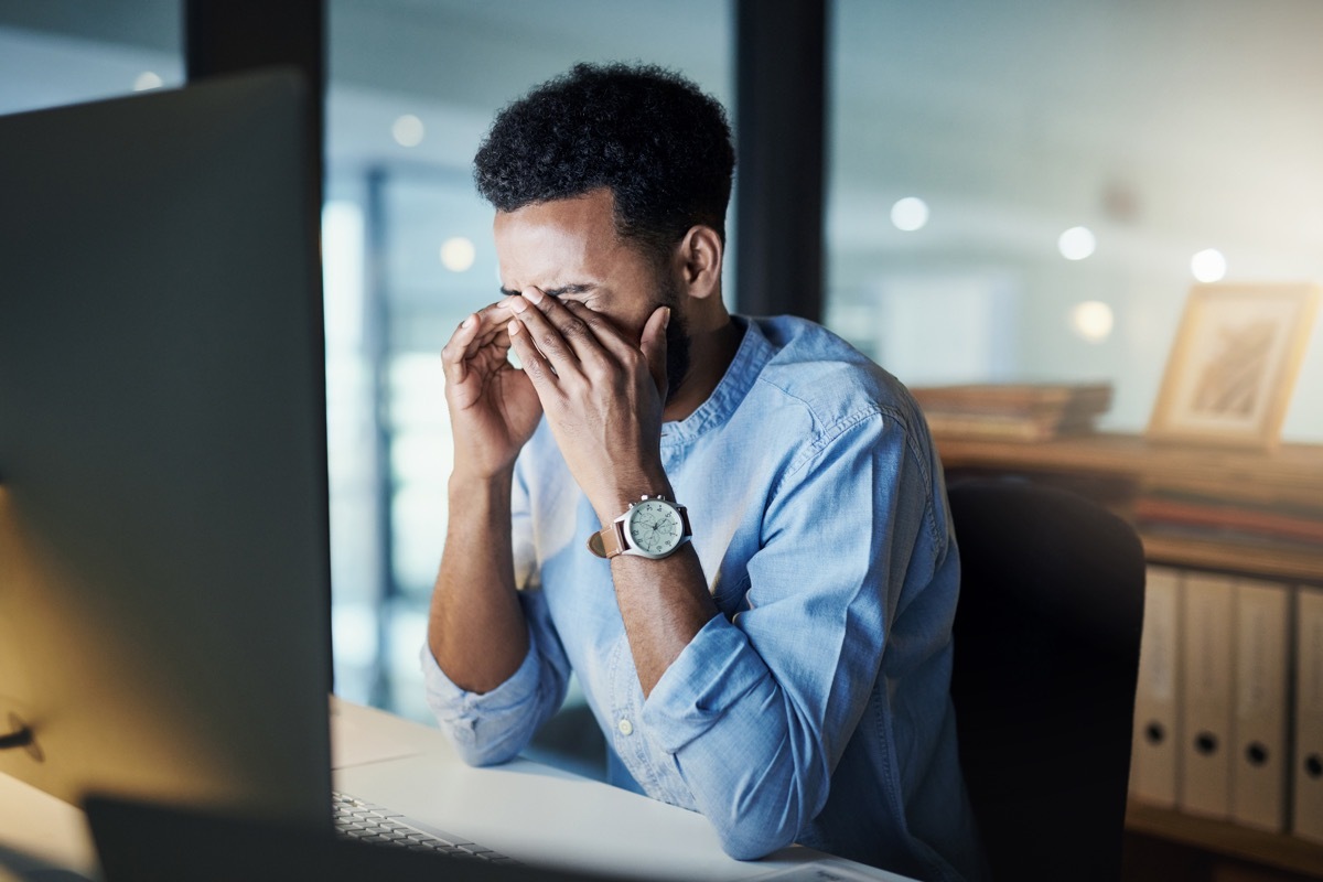 Shot of a young businessman rubbing his eyes while working on a computer in an office at night