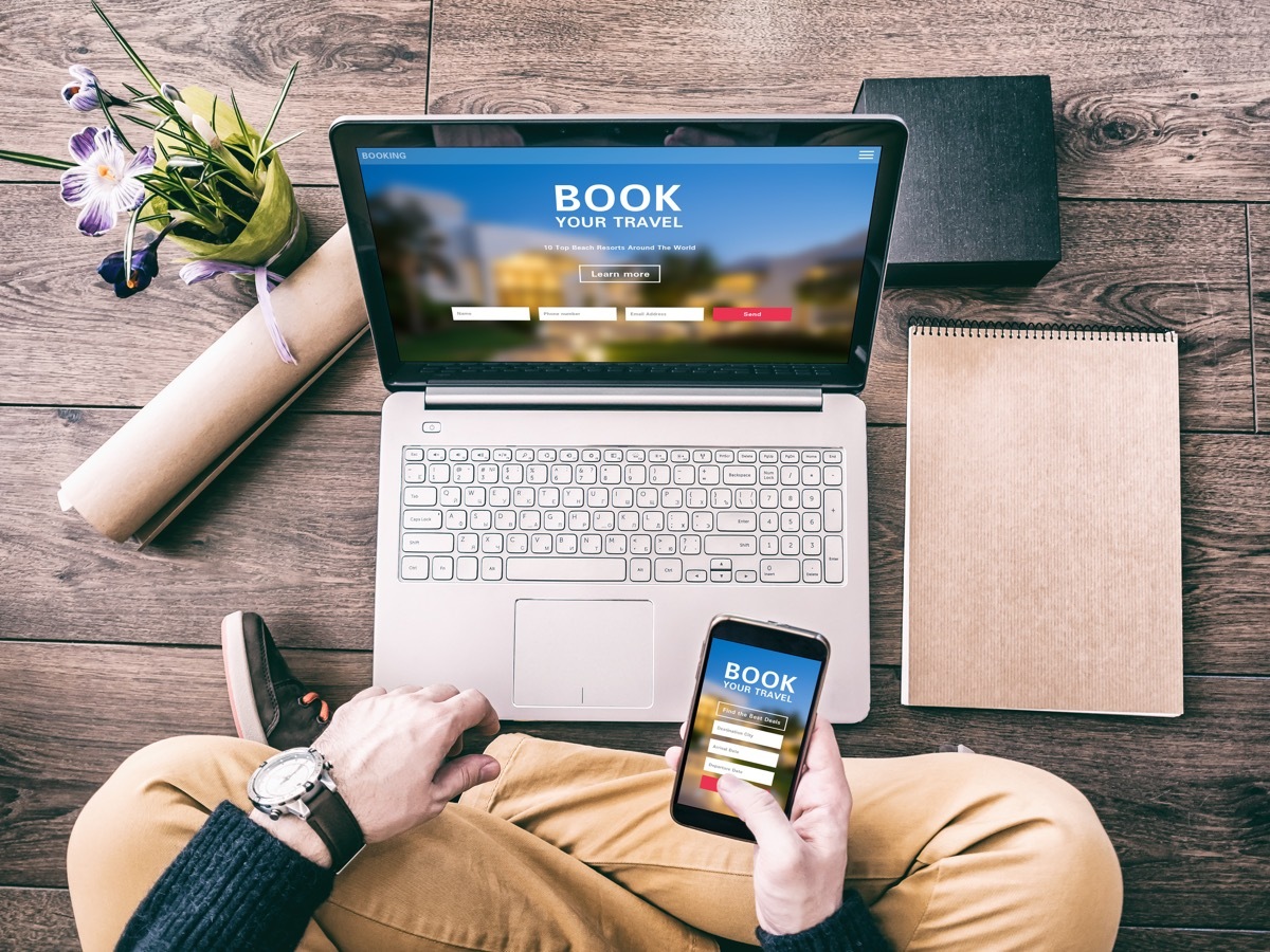 Man using a laptop and smartphone for booking hotel online. Tour reservation, Screen graphics are made up.