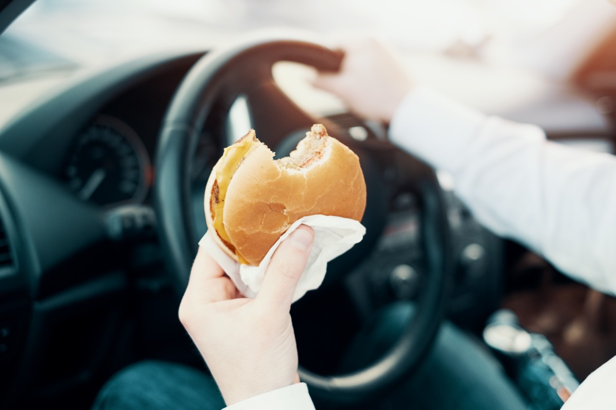 Man eating an hamburger and driving seated in his car