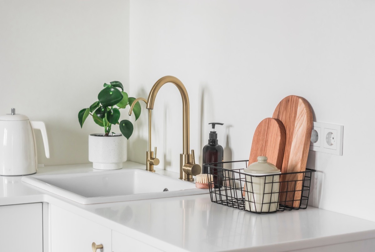 Beautiful bright interior of the kitchen in a minimalist style - kitchen furniture with ceramic sink, brass faucet, cutting boards, kettle and homemade flower on the surface