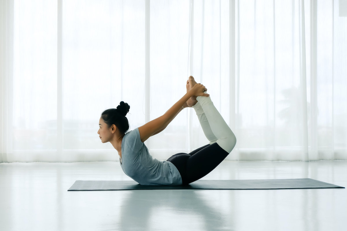 Side view portrait of Beautiful Asian woman working out in fitness club or at home, doing yoga or pilates exercise. Dhanurasana, Bow pose,Full length, Concept of healing body and spirit