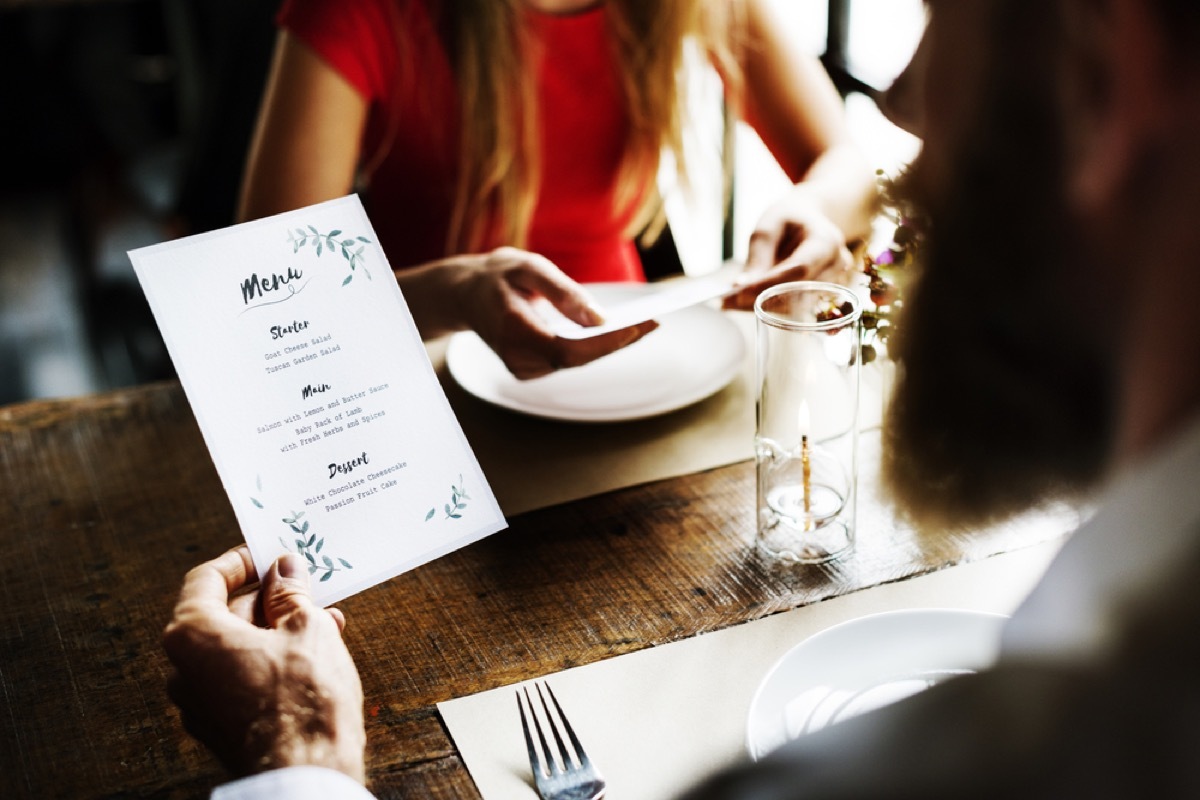 white man reading menu at dinner with woman in red dress