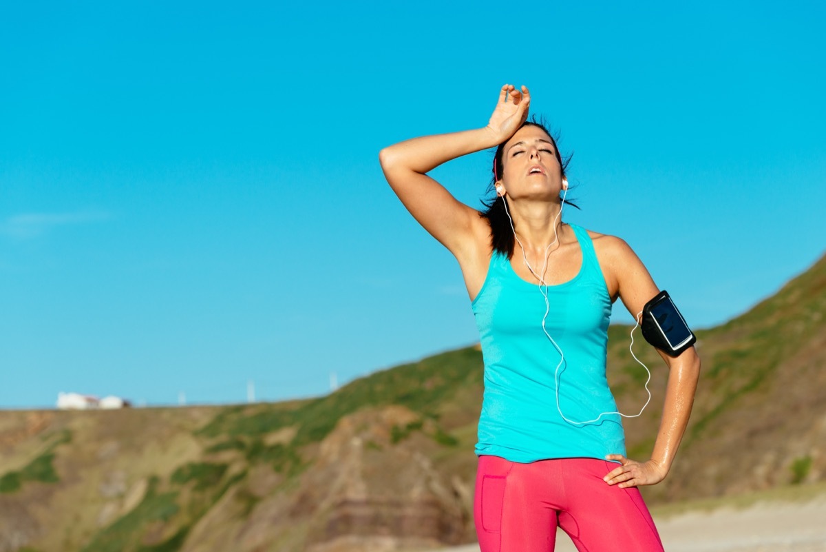 Woman tired of running outdoors putting hand on head while wearing blue tank top and red pants