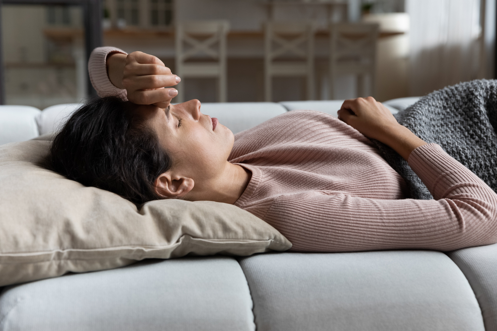 A young woman lying on the couch with symptoms of COVID, the flu, or a cold