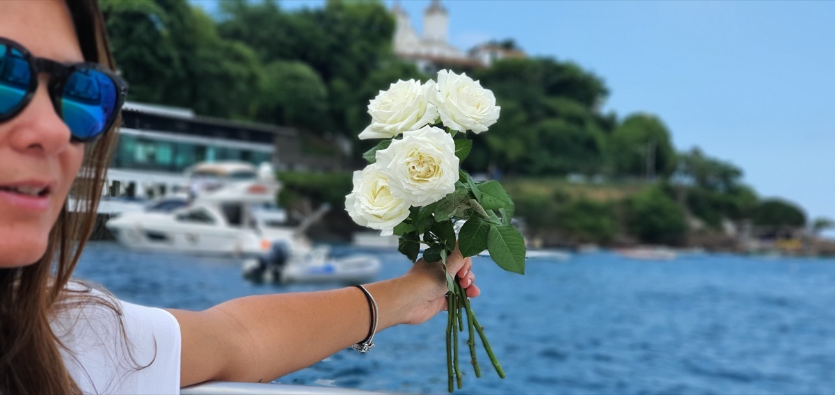 Young woman dropping white flowers into ocean