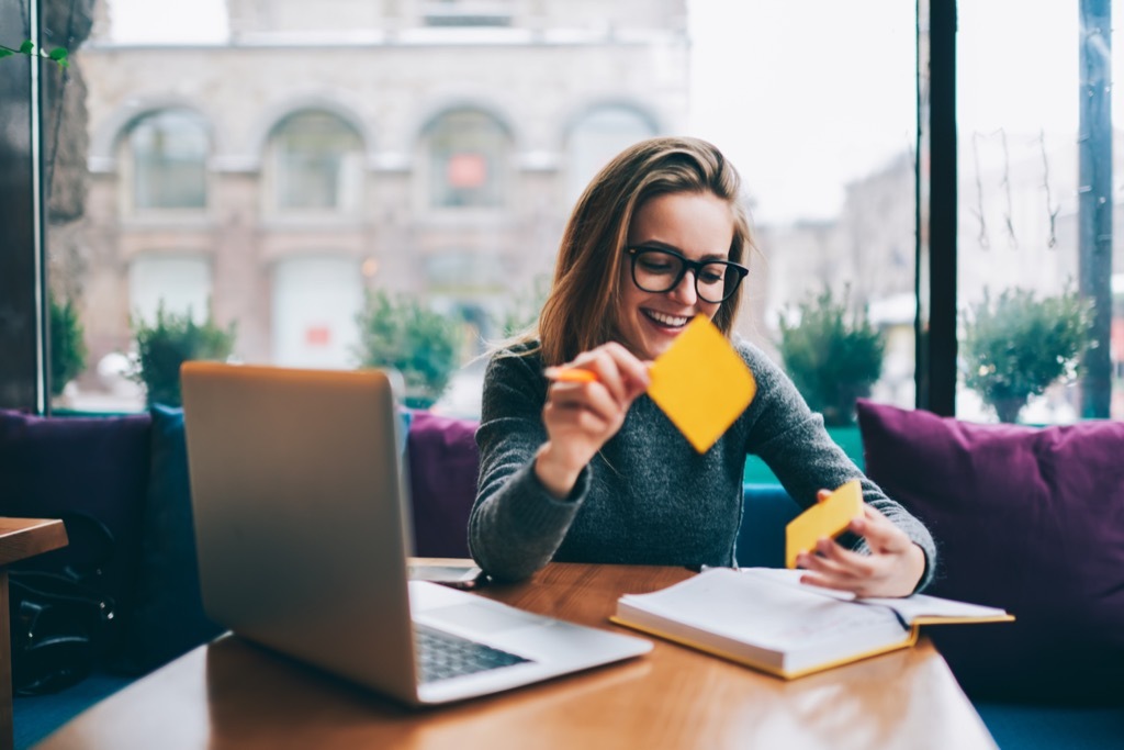 a woman sitting in front of a laptop in a cafe putting sticky notes in a book