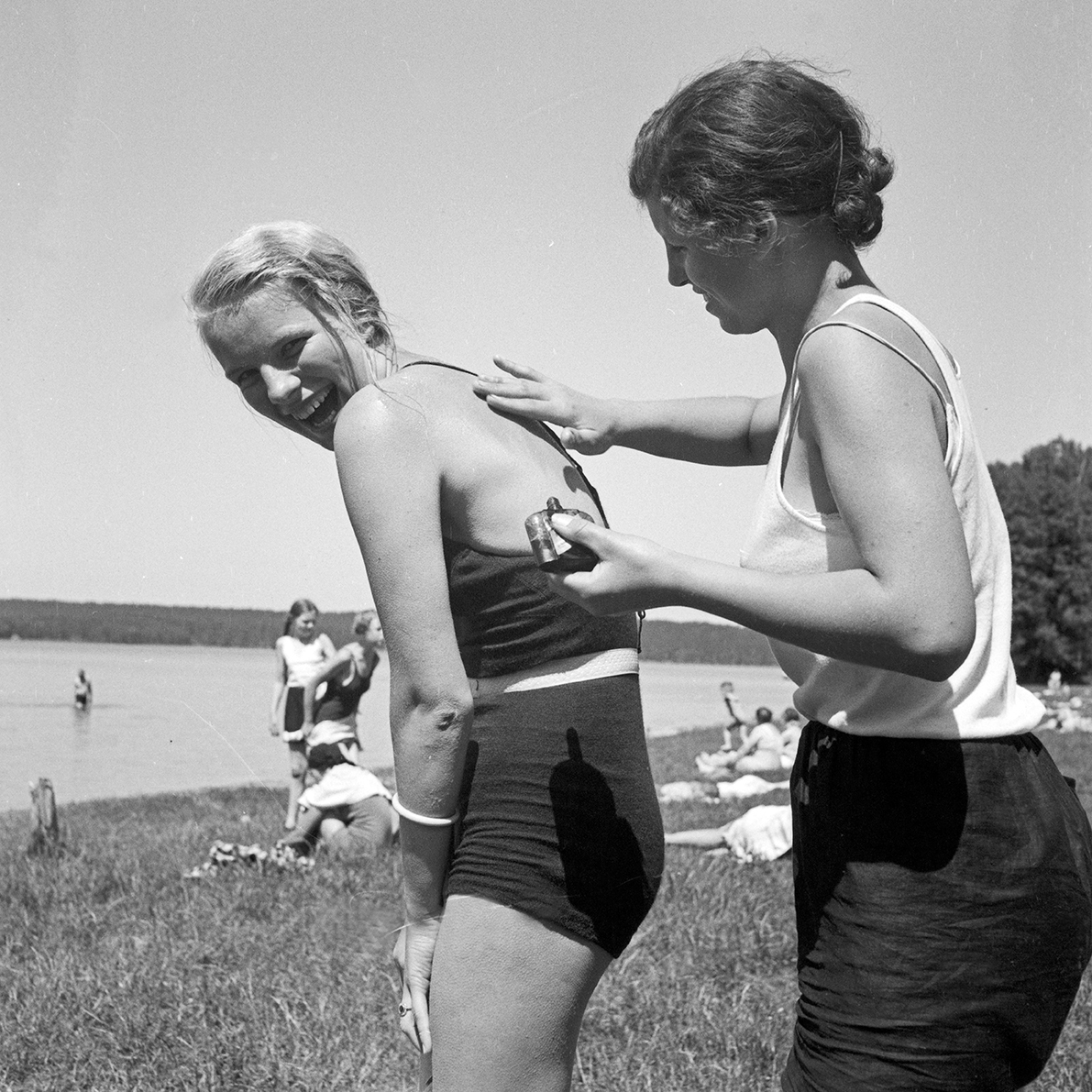 a woman puts sunscreen on her female friend at the beach