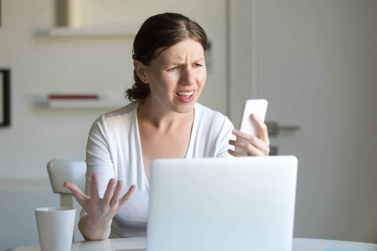 A young woman looks angrily at her cell phone while reading a text message