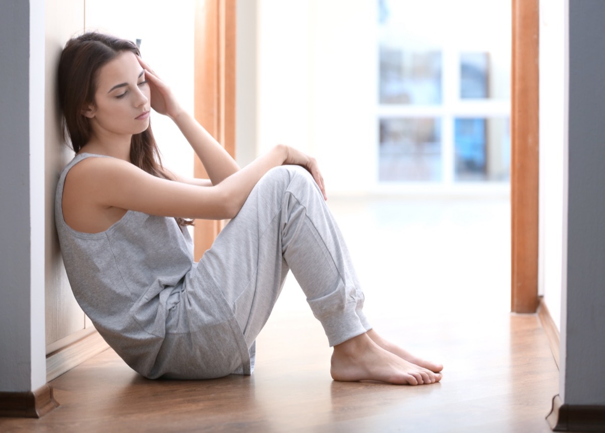 Depressed young woman sitting on floor at home