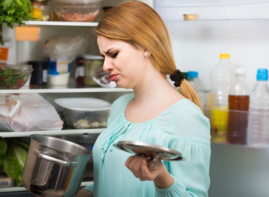 woman smelling spoiled food from pot holding lid