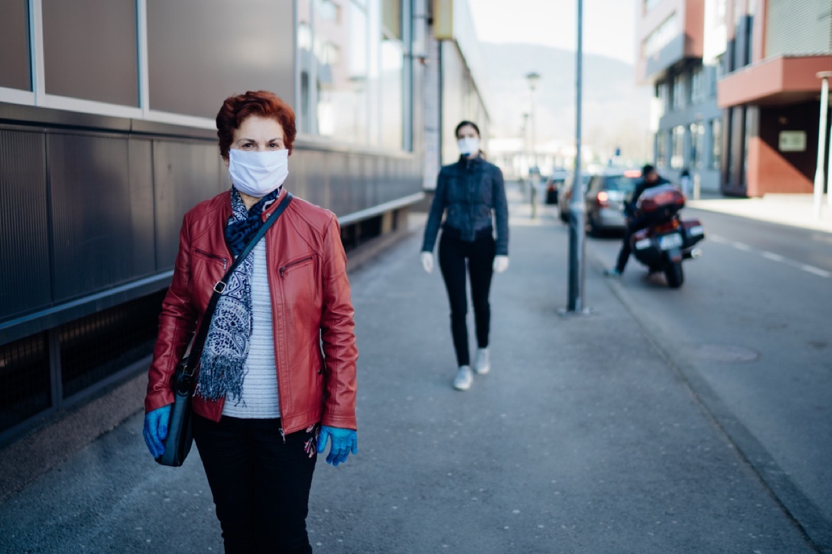 older white woman with face mask walking on sidewalk with another woman walking behind