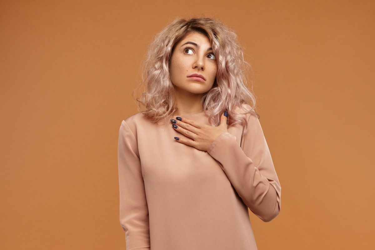 Portrait of confused emotional bug eyed young Caucasian female holding hand on her chest and looking up with clueless indecisive facial expression