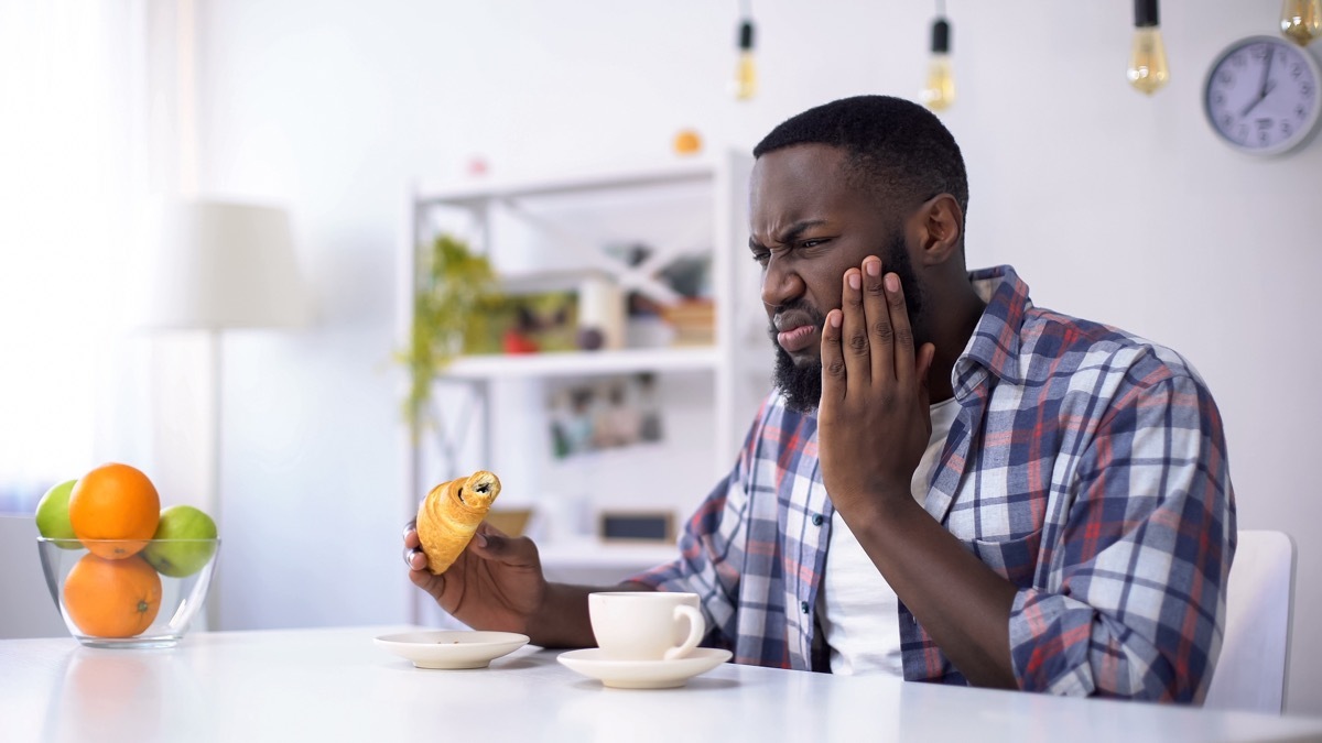 man feeling tooth ache from sweet food, eating croissant with coffee