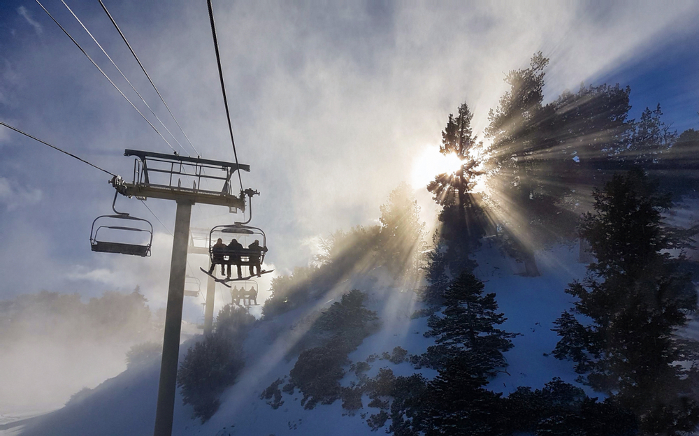 A charlift with three riders heading up a ski slope