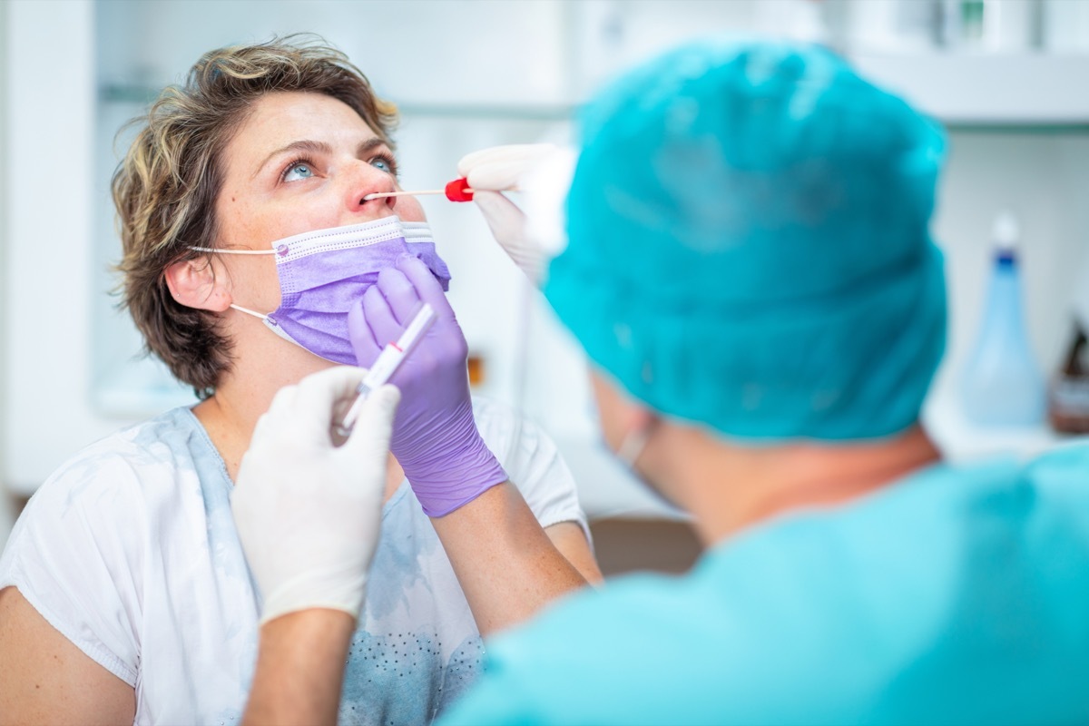 Doctor in protective workwear taking nasal swab from female patient with face mask