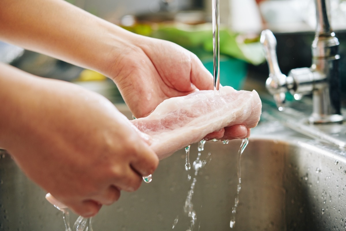 Man washing meat in sink