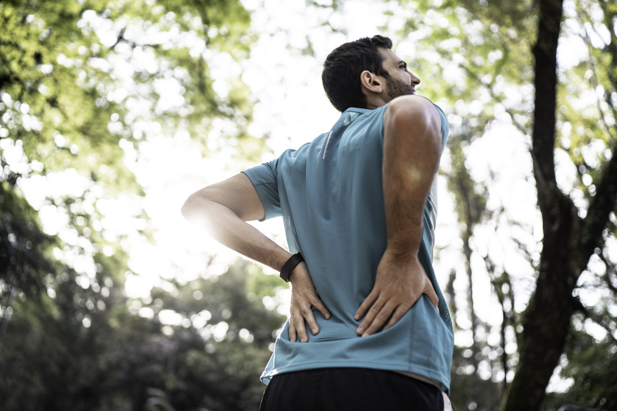 Man holds lower back in pain at a park