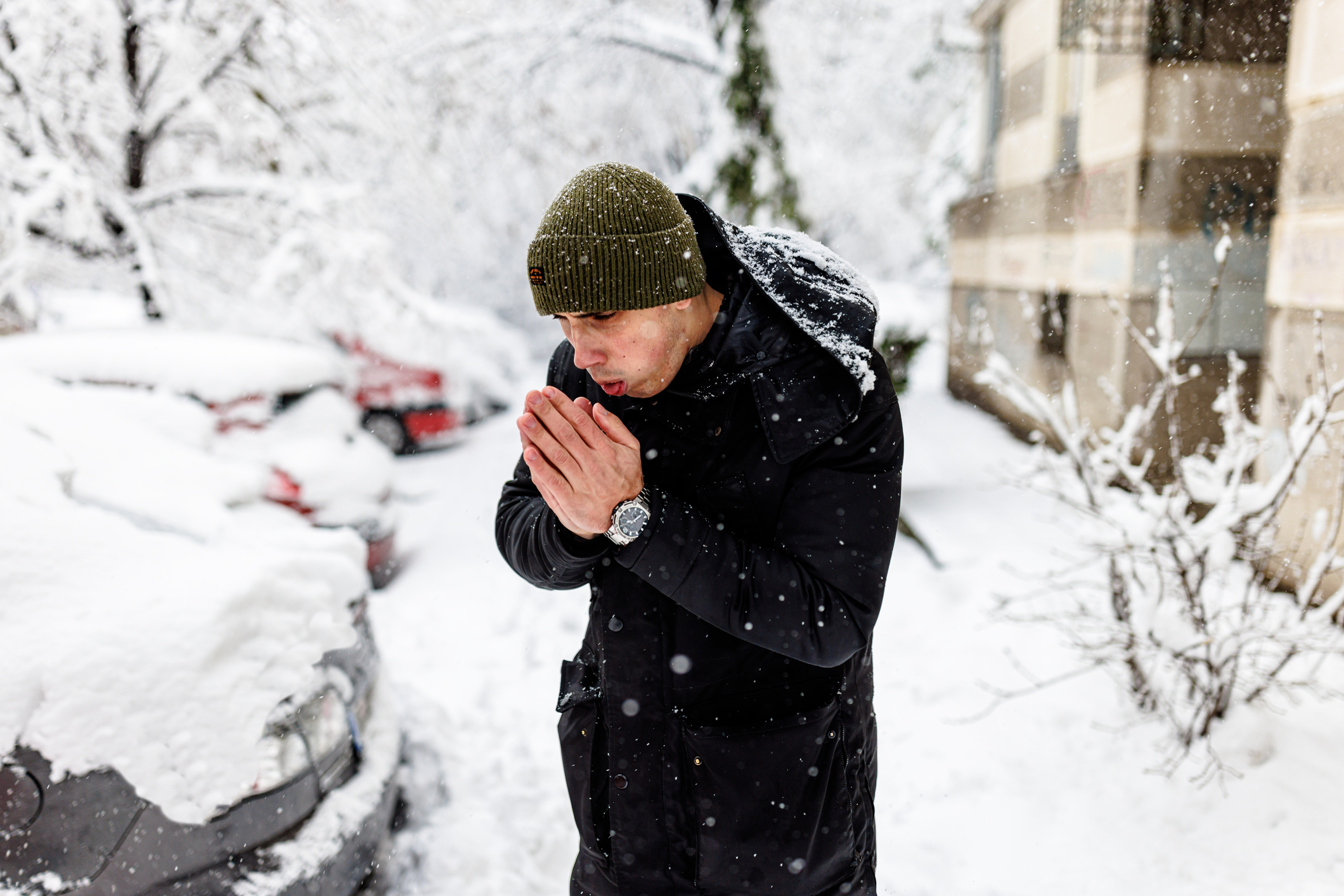 A man trying to warm his hands while standing outside in a snow storm