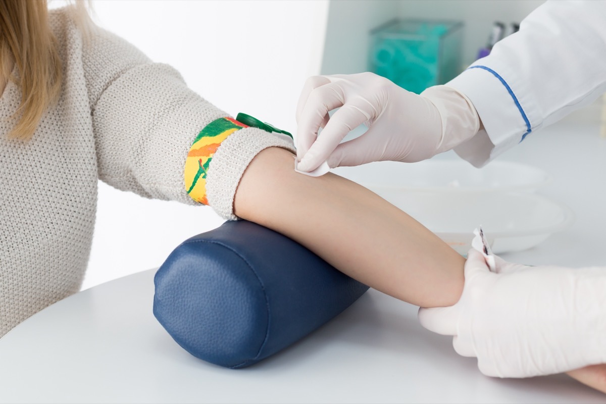 Preparation for blood test with beautiful young blond woman by female doctor in white coat medical uniform on the table in white bright room. Nurse rubbing a hand sterile patient tissue.