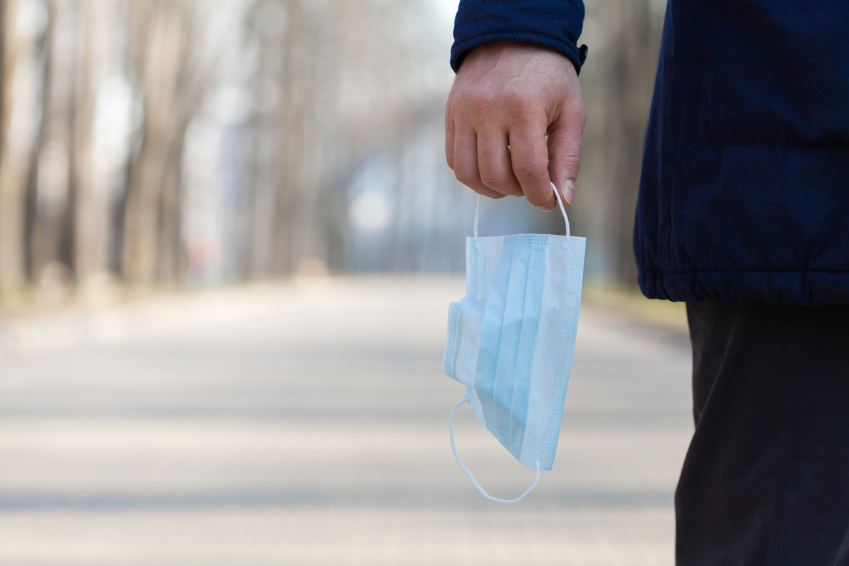 closeup of hand holding medical mask while walking in park amid coronavirus pandemi