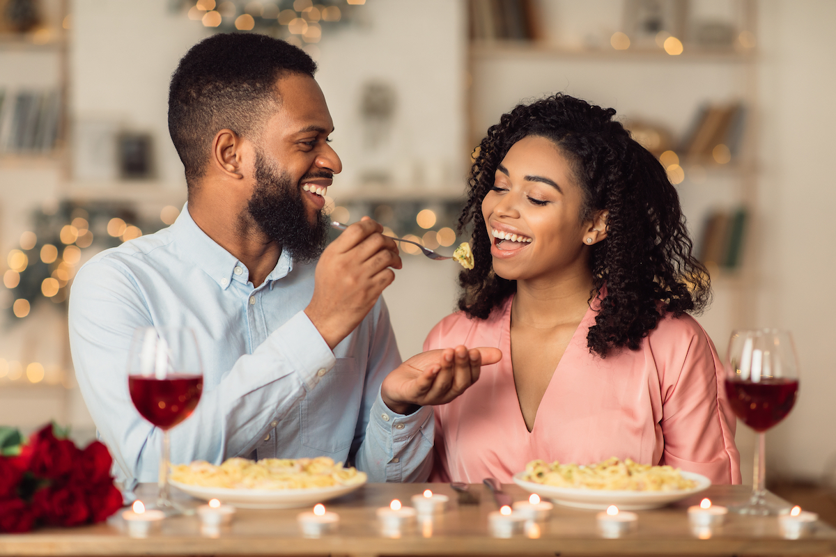 man feeding food to a woman at the table with wine glasses in front of them