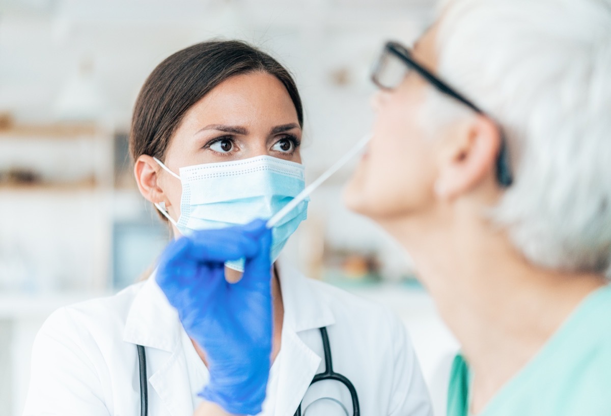 Doctor with protection gloves doing Coronavirus nasal swab test on senior female patient