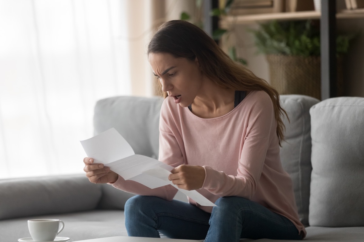 Angry woman sitting on couch at home holding letter reading awful news about company job refusal feels frustrated negative emotions face expressions, college admission or bank loan rejection concept